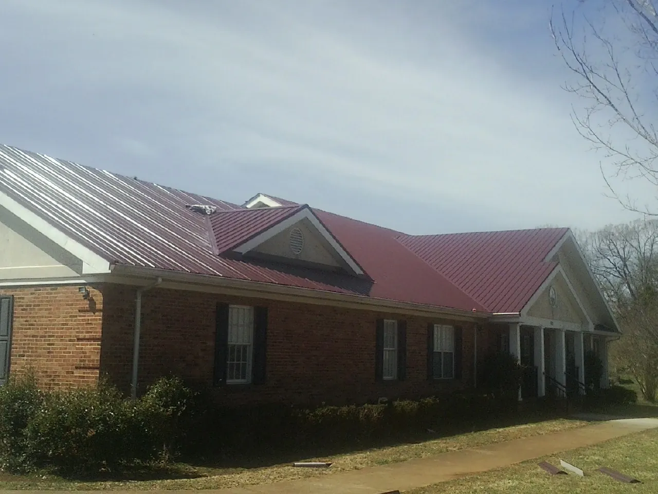 Red metal roof with gabled entries on a long brick building, from a Hail Damage Roof Repair job in East Berlin