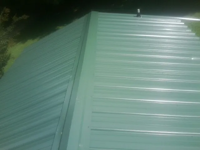 New green metal panels meeting at the ridge of a roof — Flat Roof Repair work by our crew in East Berlin
