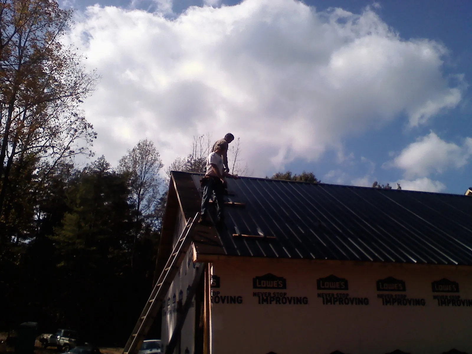 Roofer fastening dark metal panels high against a cloudy sky, from a Roof Inspection job in East Berlin